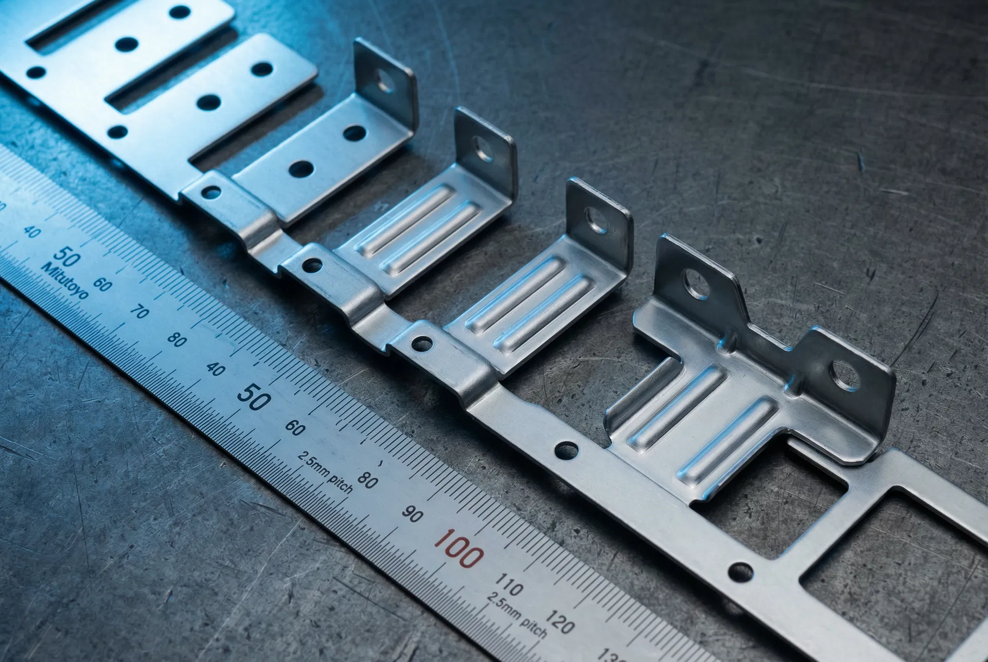 5052-H32 aluminum progressive die strip — 6-stage blanking and forming, clean shear edges, Technical Blue lighting